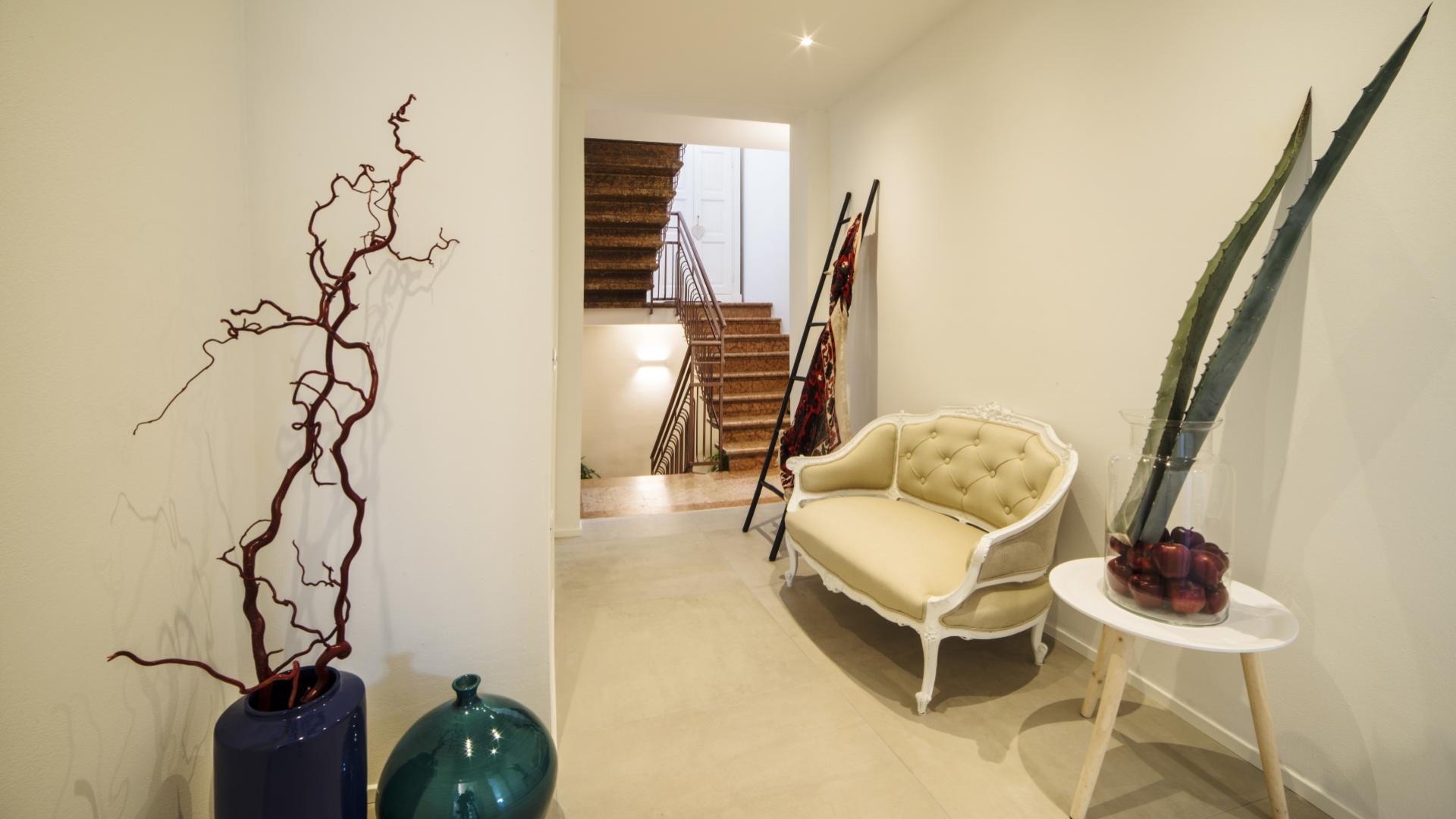 Ingresso elegante con divano, piante decorative e scala in legno.