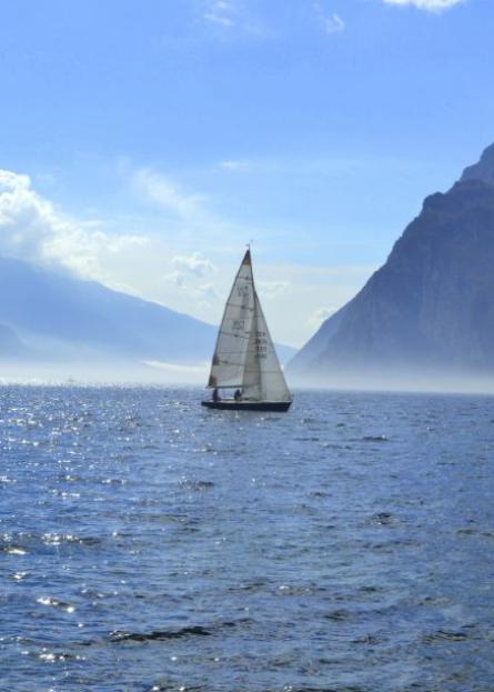Barca a vela solitaria naviga su acque calme, circondata da montagne e cielo azzurro.